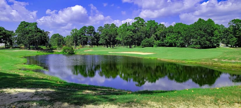 Lush golf course in Limbe with a reflective pond, sand bunkers, and surrounding trees under a bright blue sky.