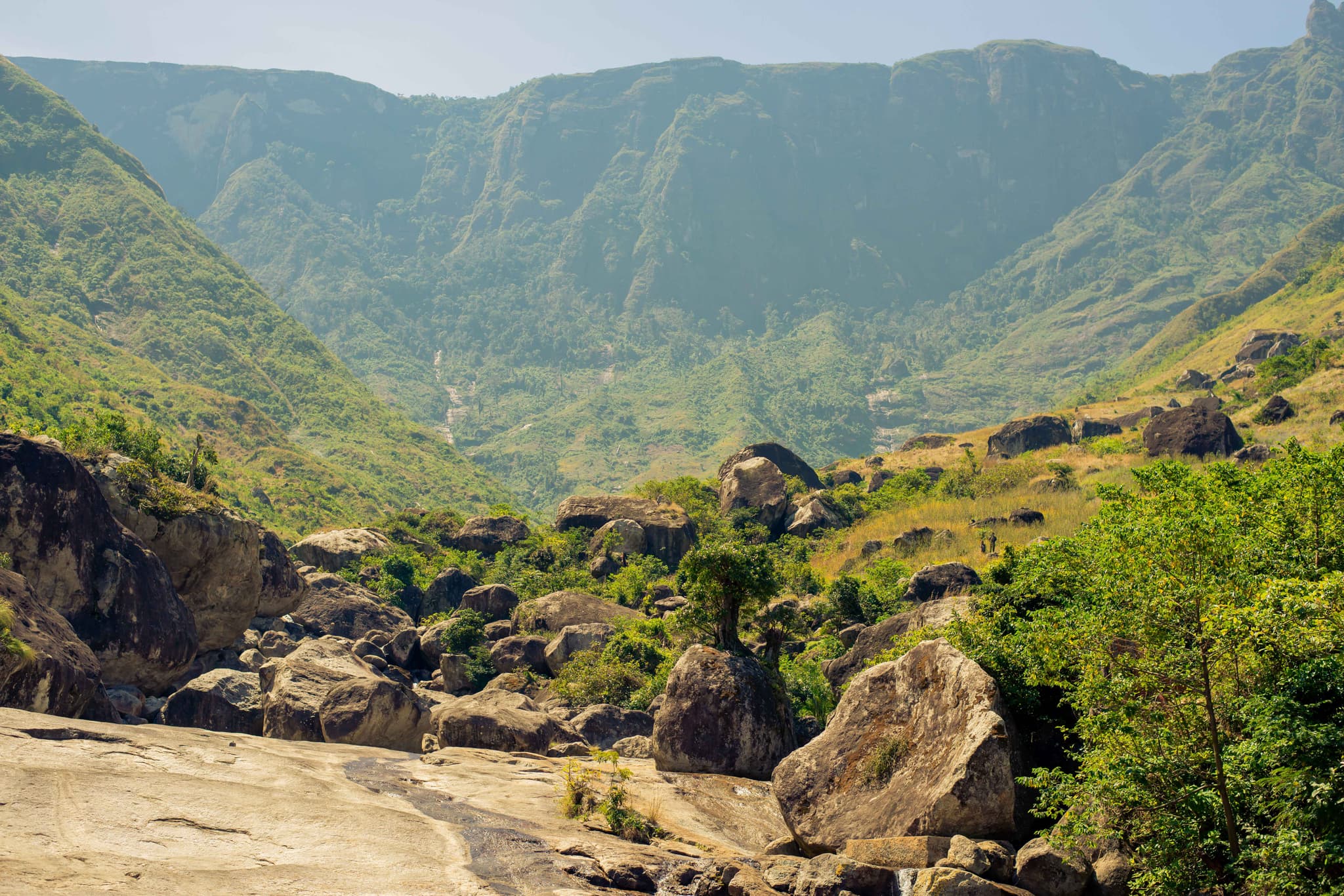 Rocky mountain terrain surrounded by greenery and cliffs under bright daylight, perfect for hiking and exploration.