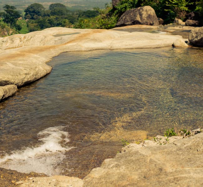 Clear natural pool surrounded by smooth rocks and greenery, perfect for a refreshing outdoor dip.