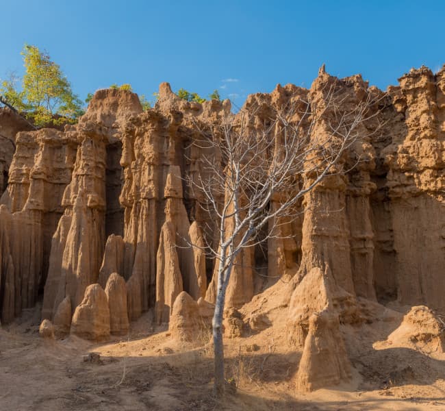 Majestic natural rock formations with tall, sculpted pillars and rugged terrain under clear blue skies.