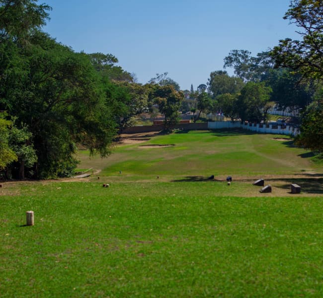 Scenic view of a lush green golf course surrounded by tall trees on a sunny day in Blantyre, Malawi.